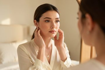 Jeune femme au maquillage naturel et élégant, se préparant avec soin dans une chambre baignée de lumière douce.