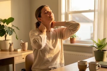 Une femme se détend chez elle après le télétravail en étirant doucement sa nuque et ses épaules près de son espace de travail.